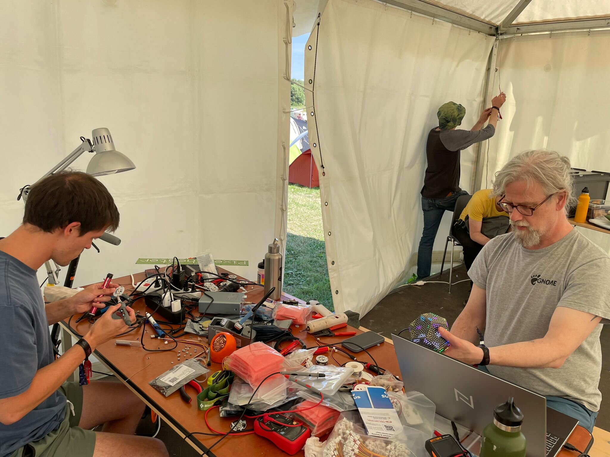 People working on electronics around a crowded workbench inside the Pixel Theater tent